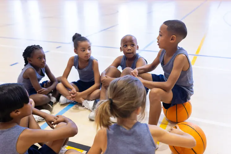 Young children participating in a basketball activity inside a school gymnasium